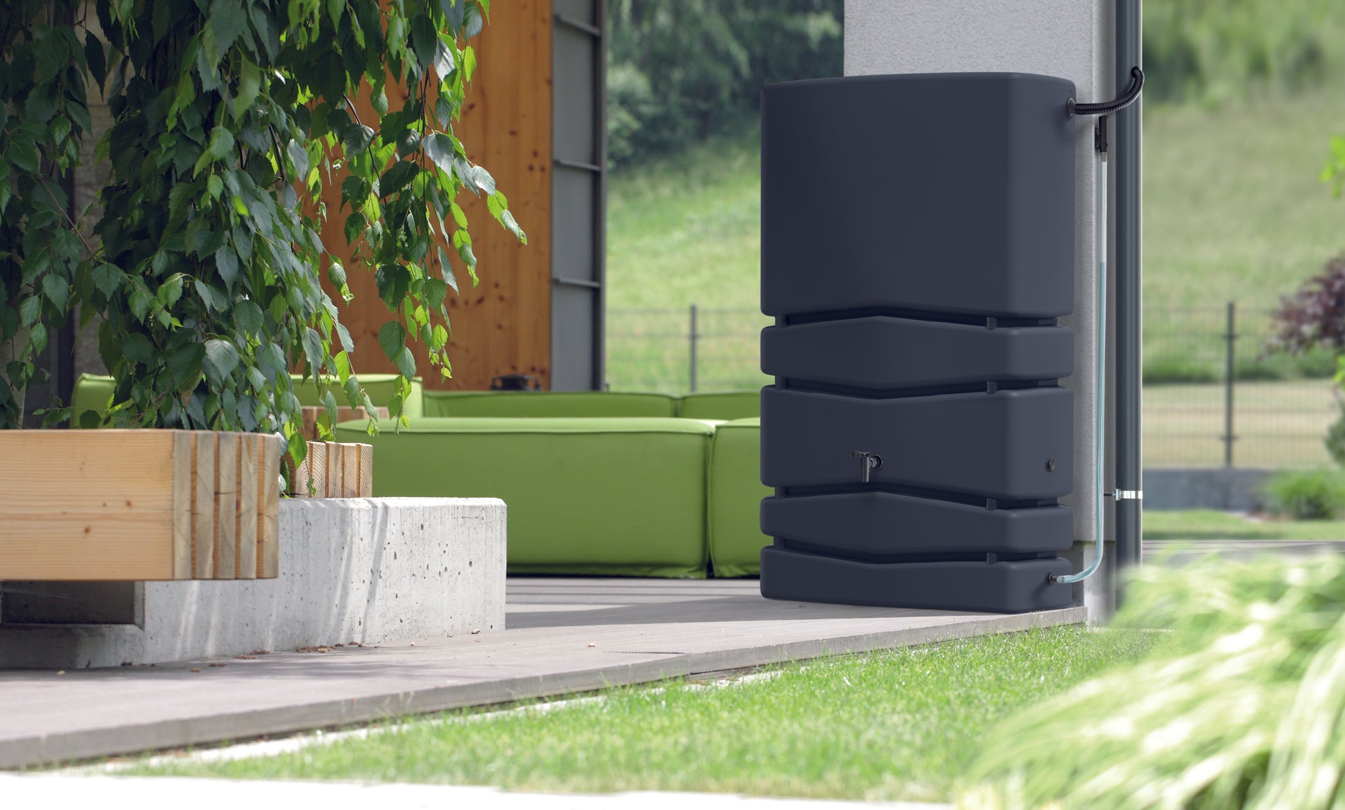Ein schwarzer YourCasa Regentonne Aqua Silo 350/450 und 650 Liter steht neben einer grünen Couch, bereit für die Regenwassernutzung.