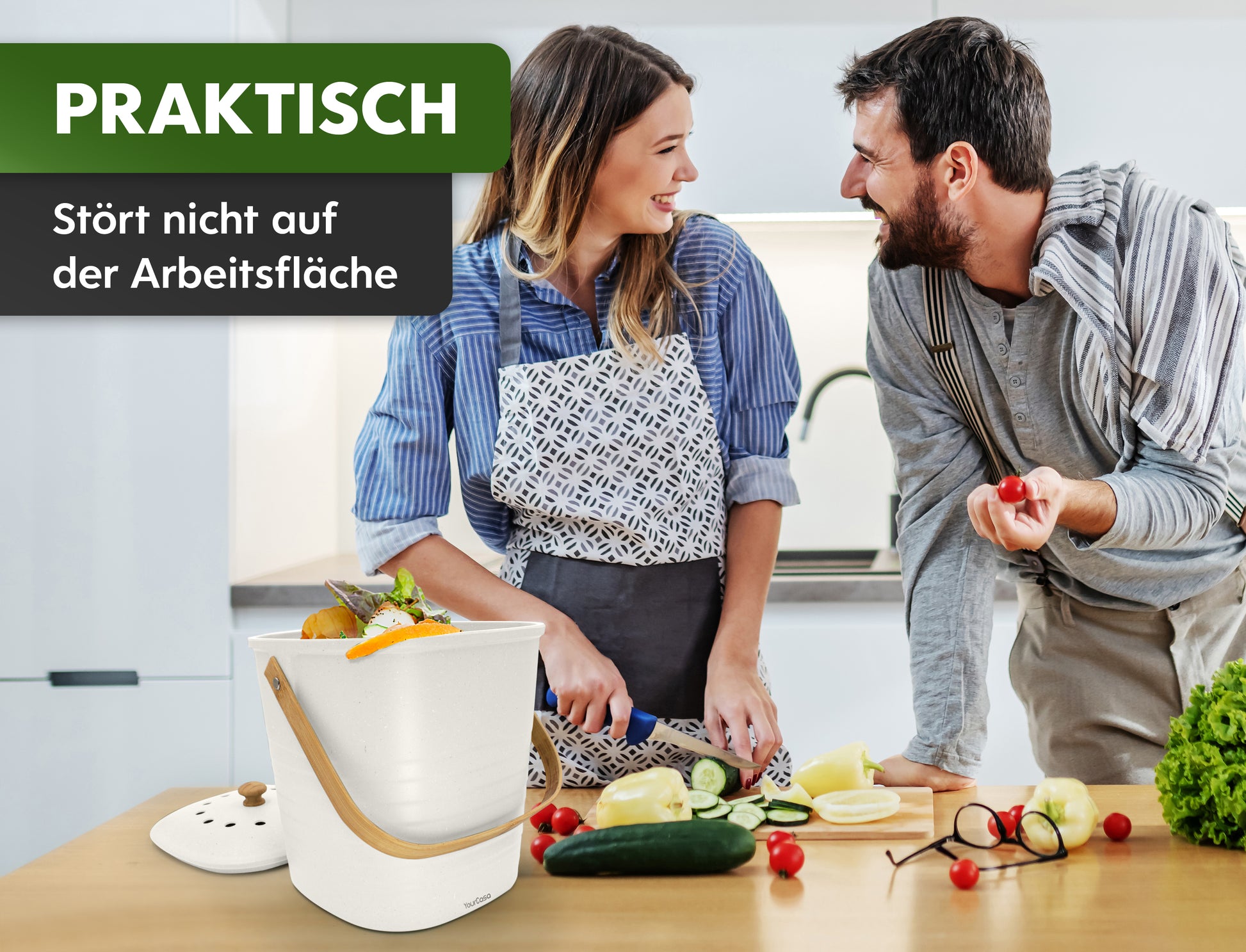 Zwei Personen sind in einer Küche mit der gemeinsamen Essenszubereitung beschäftigt. Im Mittelpunkt steht ein kompakter „YourCasa® Komposteimer“, der als praktisch und unaufdringlich am Arbeitsplatz hervorgehoben wird.