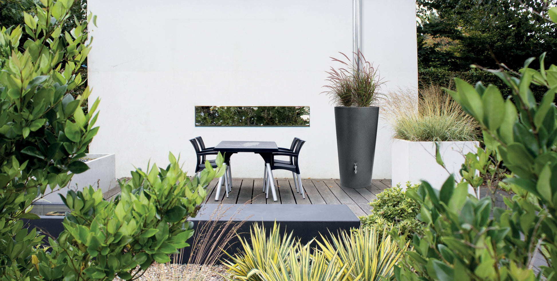 Moderne Außenterrasse mit Esstisch-Set, dekorativen Pflanzen und einer YourCasa Regentonne 150 Liter [Aquaform Flower] – mit Pflanzkübel und Metallgewinde.