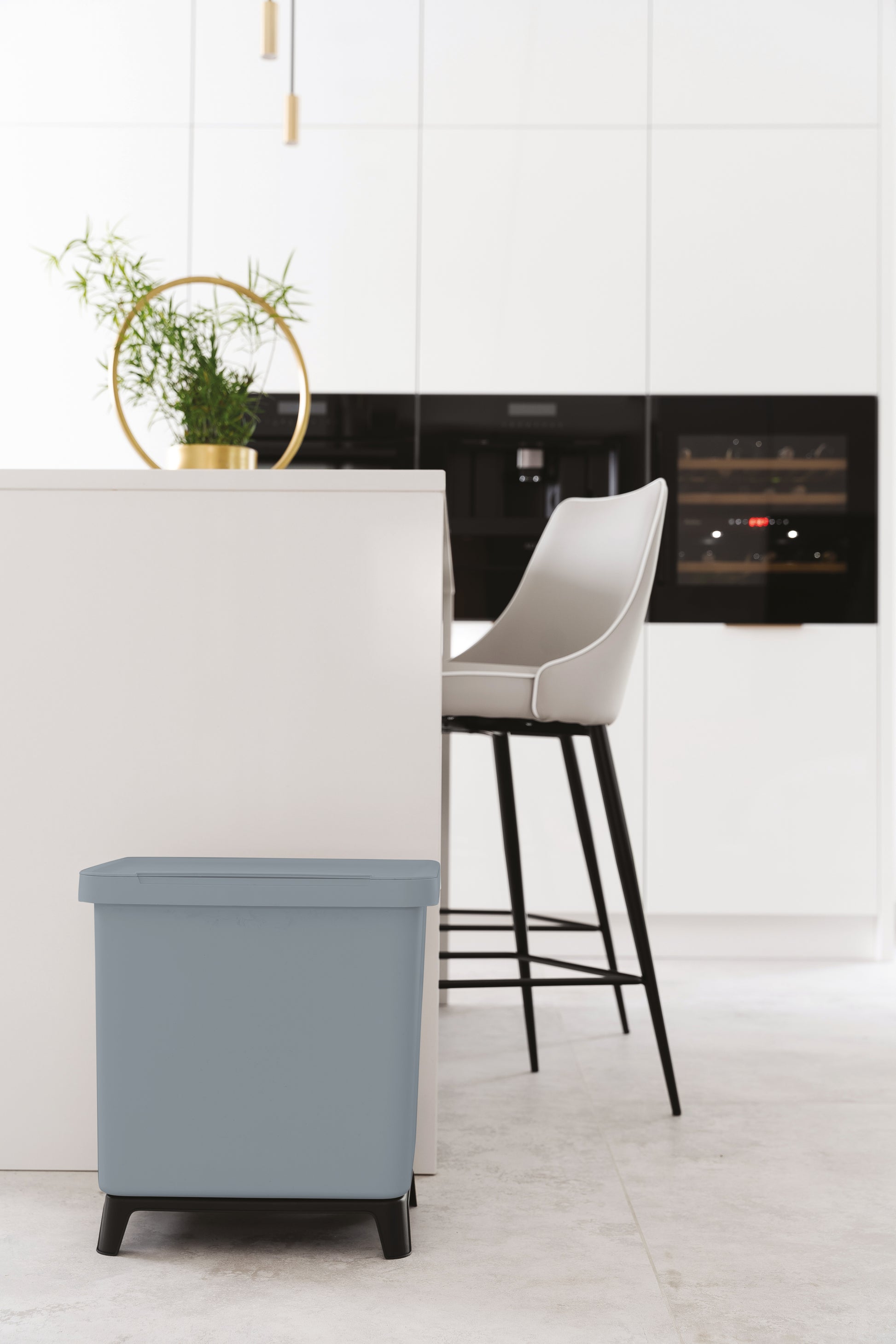 Eine moderne Küche mit einem blauen YourCasa® Mülltrennsystem mit 2-4 Fächern [20-40L] im Vordergrund und einer weißen Arbeitsplatte mit einem Backofen und einem Barhocker.