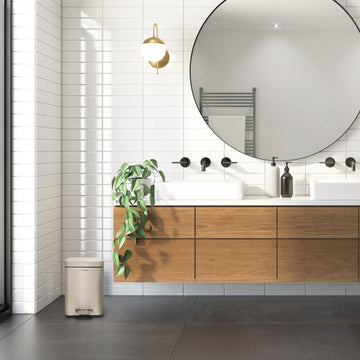 Ein Badezimmer mit rundem Spiegel und einem Yourcasa-de Edelstahl-Mülleimer.
