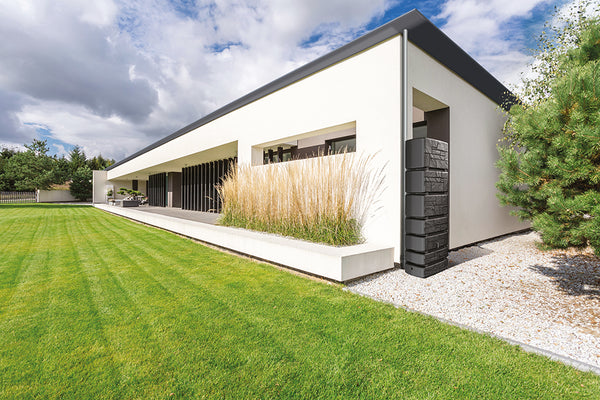 Ein modernes Haus mit Turmstein: Moderner Regenwasserspeicher in einer Rasenfläche.